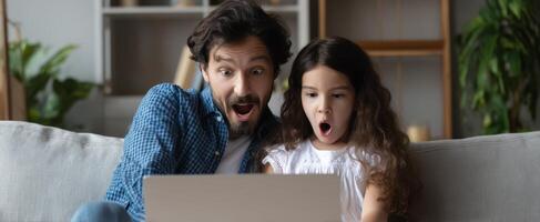 The father and daughter share a moment of surprise while using a laptop. photo