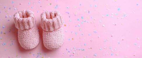 The delightful pink knitted booties surrounded by shimmering confetti on a soft background. photo