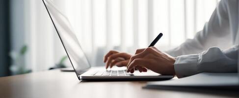 The focused individual typing on a laptop with a pen in hand photo
