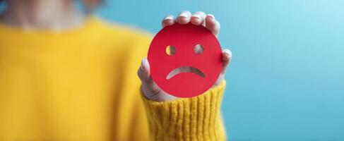 The red sad face held by a person expressing negative emotions. photo