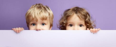 The curious children peeking over a pastel backdrop with bright expressions. photo