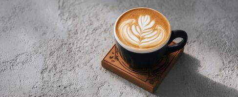 The beautifully crafted latte art in a black cup on a wooden coaster. photo