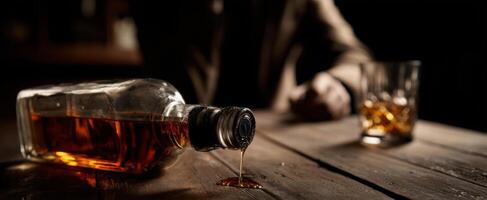 The whiskey bottle spills amber liquid on a rustic wooden table. photo