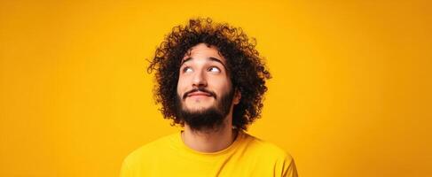 The cheerful man with curly hair looking up against a vibrant yellow background. photo