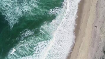 drone zenithal view aerial footage flying over a beach parallel to the water, day of surf and foam. video