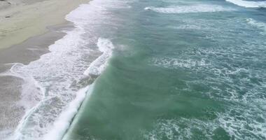 drone view aerial footage flying over a beach parallel to the water, day of waves and foam. Sea background video