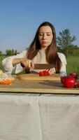 A village girl cuts vegetables on the table, preparing for a festive dinner in honor of the harvest. The cook cuts the tomatoes into small pieces. Vertical. video