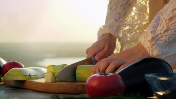 skillful female chef, working in culinary industry, skillfully slices zucchini into uniform cubes using sharp knife on cutting board while preparing dish outdoors. video