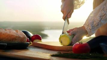 Large zucchini is sliced into small pieces, along with other vegetables, to create appetizing, organic vegetarian salad against backdrop of beautiful natural scenery. video