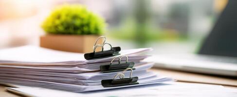 The organized stack of documents with binder clips and a touch of greenery. photo