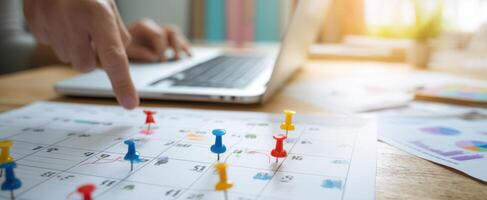 The calendar filled with colorful pins and a person organizing tasks on a laptop. photo
