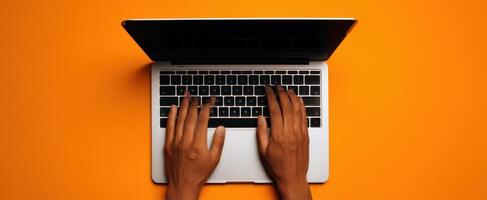 The laptop with hands typing on a vibrant orange background. photo