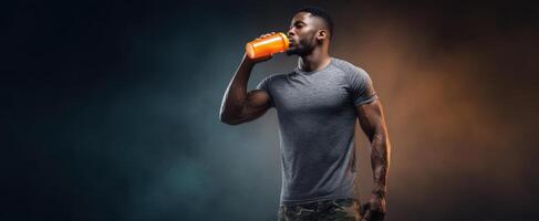 The fit man enjoying a refreshing orange energy drink in a studio setting. photo