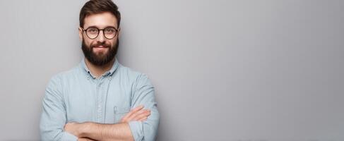 A man with a beard and glasses standing in front of a gray wall photo