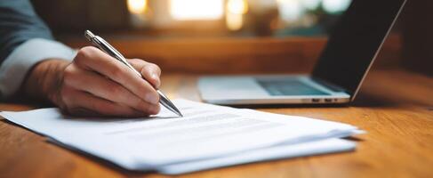 The Hand Writing on Documents Next to a Laptop in a Cozy Workspace photo