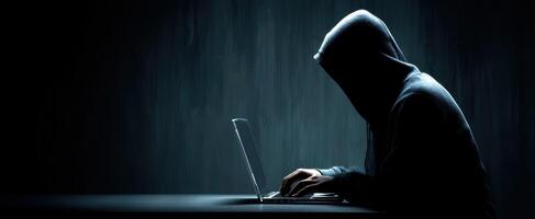 The hooded figure intensely focused on a laptop in a dark environment. photo