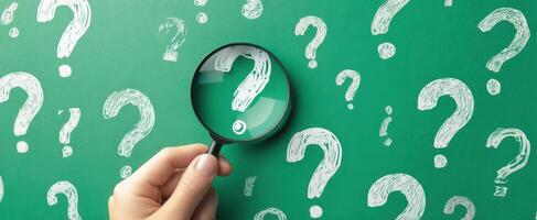 The Hand Holding a Magnifying Glass Over Question Marks on a Chalkboard Background photo