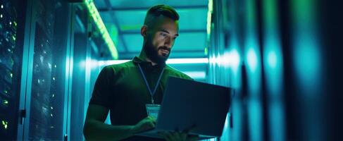The focused IT professional working on a laptop in a server room. photo