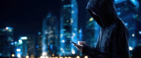 The hooded figure using a smartphone in a vibrant city at night photo