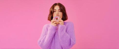 The young woman enjoying a colorful donut against a vibrant pink background. photo