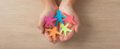 Hands holding colorful paper people on wooden table photo