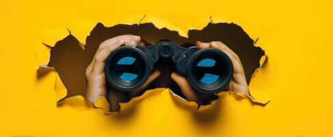 The Hands Holding Binoculars Peering Through a Torn Yellow Background photo