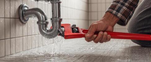 The plumber fixing a leak under the bathroom sink with a wrench. photo