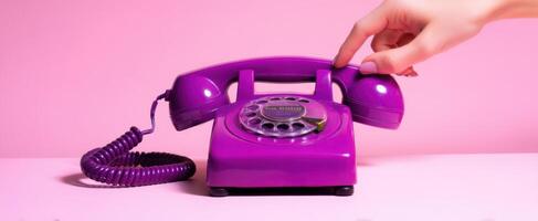 The stylish vintage purple telephone with a hand reaching to dial. photo