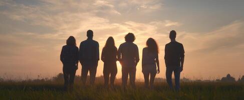 The group of friends silhouetted against a beautiful sunset in a grassy field. photo