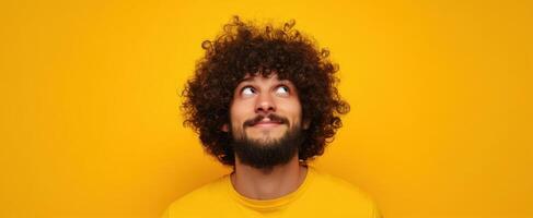 The young man with curly hair enjoying a moment of imagination against a yellow backdrop. photo