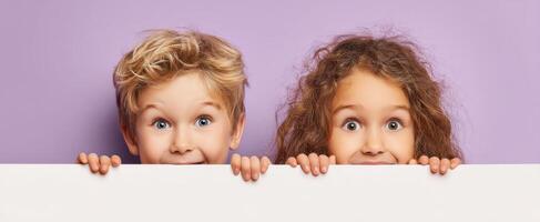 The cheerful children hiding behind a blank banner with playful expressions. photo