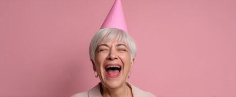 The joyful elderly woman celebrating with laughter in a pink party hat. photo
