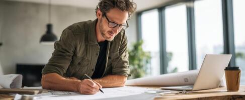 The architect analyzing blueprints in a modern workspace with laptop and coffee. photo