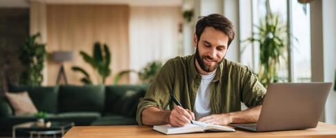 The man writing in notebook while sitting at modern home workspace. photo