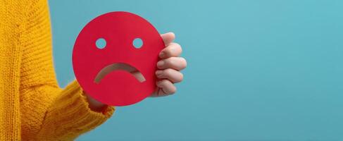 The hand holding a red sad face symbol against a colorful background. photo