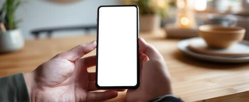 The smartphone held in hands with a blank screen on a wooden table photo