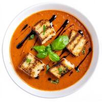 An image of a bowl of creamy tomato basil soup, topped with grilled cheese croutons and a drizzle of photo