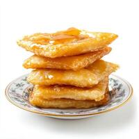 A close-up of a stack of fluffy sopapillas, deep-fried pastries drizzled with honey and cinnamon, served as a sweet treat, presented on a decorative plate, isolated on clean white background. photo