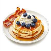 A plate of fluffy pancakes, topped with fresh blueberries, a drizzle of maple syrup, and a dollop of whipped cream, served with a side of crispy bacon. The pancakes, with their light and airy texture, photo