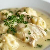 A close-up of a plate of chicken and dumplings, featuring tender chicken and fluffy dumplings in a creamy broth, garnished with fresh parsley. The chicken and dumplings, with their comforting texture photo