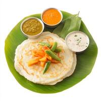 A close-up of a uttapam, with a thick pancake made from rice and lentil batter, topped with vegetables, served with sambar and chutney, arranged on a banana leaf, isolated on clean white background. photo