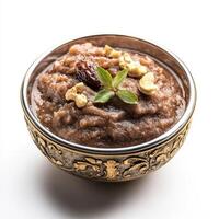 A bowl of dates halwa, with a sweet pudding made from dates, milk, and nuts, garnished with silver varak, isolated on clean white background. photo