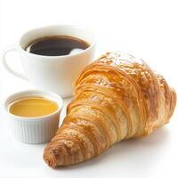 A detailed close-up of a flaky croissant, its layers glistening with butter, accompanied by a small ramekin of honey and a cup of rich coffee. The croissant, with its light, airy texture and subtly photo