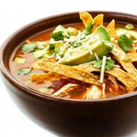 A close-up of a warm bowl of tortilla soup, with a flavorful tomato-based broth, shredded chicken, crispy tortilla strips, avocado, and cheese, served in a rustic bowl, isolated on clean white photo