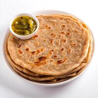 A close-up of a flaky paratha, with layers of whole wheat dough and a golden brown color, served with a side of pickle, isolated on clean white background. photo