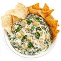 A bowl of spinach and artichoke dip, with a creamy blend of spinach, artichokes, cream cheese, parmesan cheese, and garlic, served with tortilla chips, vegetable sticks, and toasted baguette slices, photo