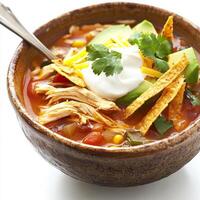 A close-up of a hearty chicken tortilla soup, with a flavorful broth, shredded chicken, crispy tortilla strips, avocado, cheese, and sour cream, served in a rustic bowl with a spoon, isolated on clean photo