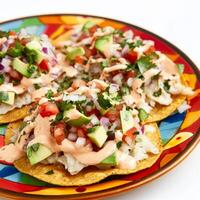 A plate of fish ceviche tostadas, crispy tostadas topped with fish ceviche, avocado, and pico de gallo, drizzled with a creamy chipotle sauce, arranged on a colorful plate, isolated on clean white photo