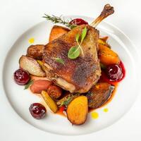 A close-up of a plate of duck confit, served with roasted root vegetables and a cherry sauce, presented on a clean white background. The duck confit, with its crispy skin and tender meat, offers a photo