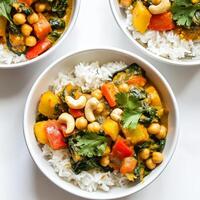A plate of vegetable and chickpea curry bowls, with tender vegetables, chickpeas, spinach, and a creamy coconut milk-based curry sauce, served over basmati rice and garnished with cilantro and cashews photo
